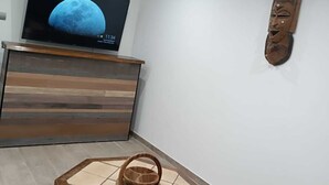 Une pièce avec un téléviseur posé sur un meuble en bois, une table en osier et un élément décoratif en bois accroché au mur.