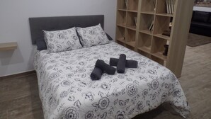 Une chambre à coucher avec un lit, des oreillers, une bibliothèque en bois et une petite plante.