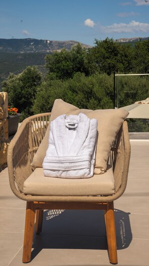 Una silla de mimbre con una toalla blanca y un cojín, ubicada en una terraza con vistas a montañas y árboles.