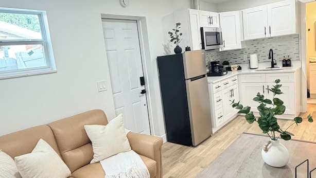 Una cocina moderna con armarios blancos, un refrigerador negro y una zona de comedor con mesa y sillas de madera.