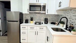 Una cocina moderna con armarios blancos, un refrigerador de acero inoxidable, un microondas y un fregadero.