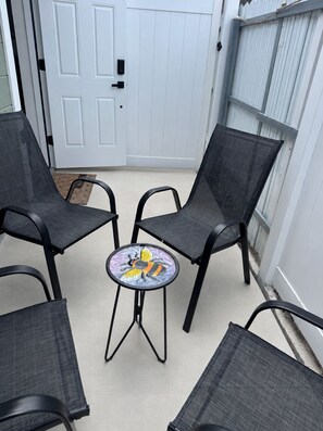 A patio with four chairs and a small table, a white door, and a white fence.