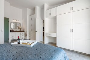 Ein Schlafzimmer mit einem Bett, einem Nachttisch mit Weinflasche und Gläsern, einer Kommode und einem großen Kleiderschrank.