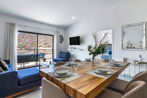 Un'area pranzo con un tavolo di legno apparecchiato per quattro persone, un divano blu e una TV montata a parete.
