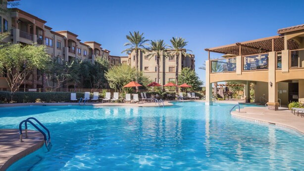 A swimming pool with lounge chairs and umbrellas, surrounded by multi-story buildings with balconies and palm trees. - Toscana Treasure! Cozy 2-bedroom condo with lots of amenities in Phoenix! (Phoenix)