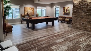 A pool table in a room with a stone accent wall, a large window, and a view of a building outside. - Toscana Treasure! Cozy 2-bedroom condo with lots of amenities in Phoenix! (Phoenix)