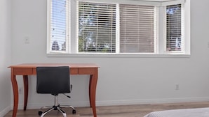 Una habitación con un escritorio de madera, una silla de oficina negra y una ventana con persianas.