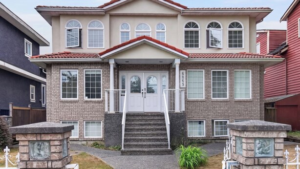 Una casa de dos pisos con fachada de ladrillo, una entrada central con escalones y una disposición simétrica de ventanas.