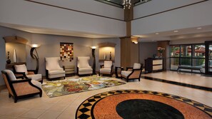 Eine großzügige Lobby mit großem Teppich, mehreren Sesseln, einer Rezeption und Blick ins Freie.
