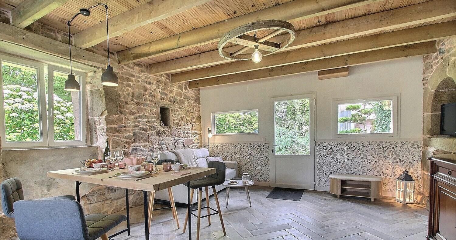 A rustic interior with exposed stone walls, wooden beams, a dining area with a table and chairs, and a cozy seating area.