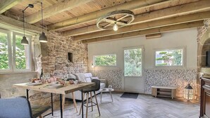 Un interior rústico con paredes de piedra vista, vigas de madera, un comedor con mesa y sillas, y una zona de estar acogedora.