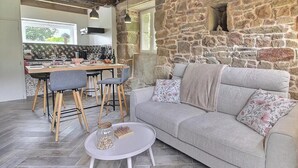 Una sala de estar acogedora con una pared de piedra, un sofá, una mesa de centro y un comedor con sillas y una mesa dispuesta para una comida.