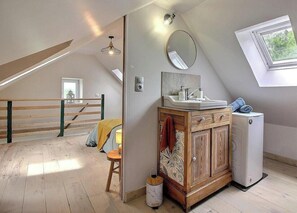 Ein Schlafzimmer im Loft-Stil mit schrägem Dach, einem Holzschrank mit Spiegel, einem kleinen Heizgerät und einem Fenster mit Blick.