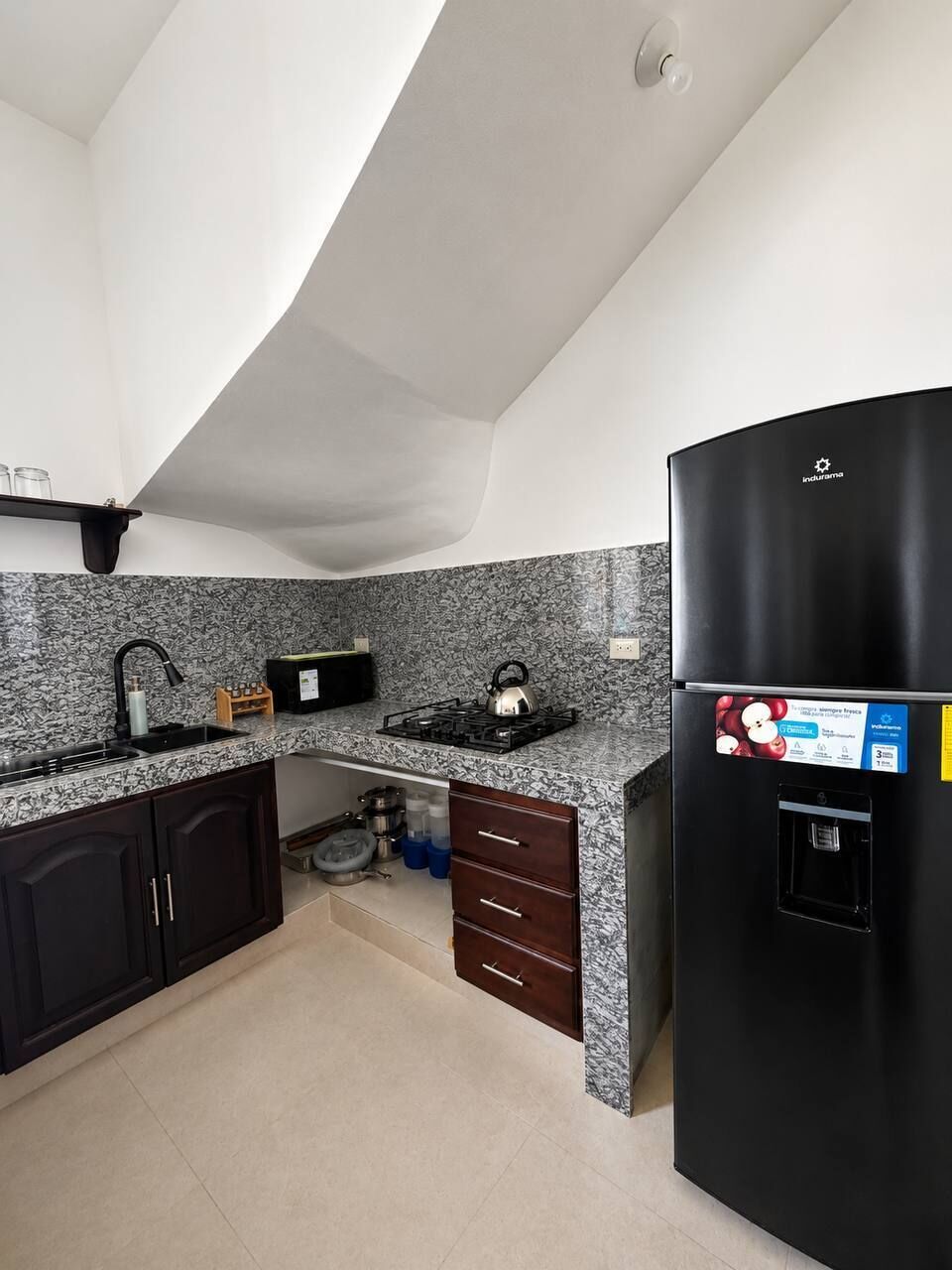 Una cocina con armarios oscuros, un refrigerador negro, una estufa a gas y una salpicadera de granito.