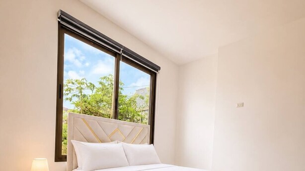 A bedroom with a bed, a nightstand, a window with a view of greenery, and a ceiling light. - MARLIN (San Cristobal)