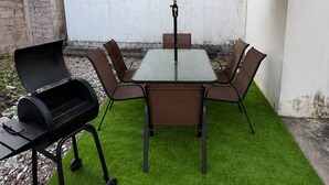 An outdoor patio with a table, chairs, a grill, and an umbrella. - MARLIN (San Cristobal)