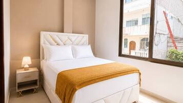 Quarto com cama, mesa de cabeceira, ar condicionado, janela com vista para edifícios e luminária no teto.