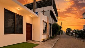 A modern residential street with a paved road, a sidewalk, and a house with large windows and a door. - MARLIN (San Cristobal)
