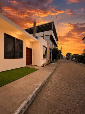 Una calle residencial moderna con pavimento, acera y una casa con amplias ventanas y puerta.