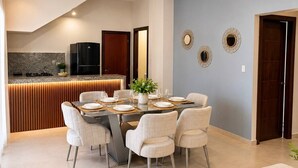 Un espace repas moderne avec une cuisine en arrière-plan, une table à manger dressée pour six personnes et un mur bleu clair agrémenté de miroirs décoratifs.