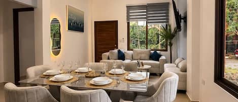 A modern dining area with a marble table, white chairs, and a sofa.