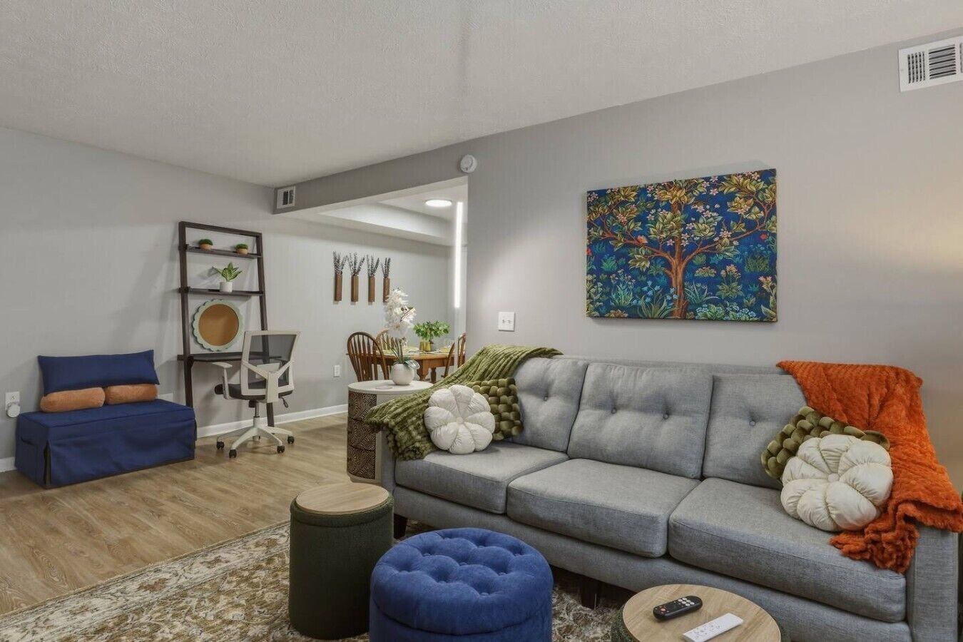 A living room with a grey sofa, blue ottoman, and a dining area with a table and chairs.