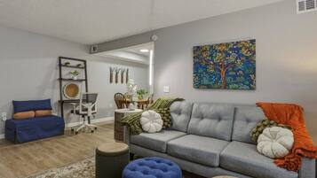 A living room with a grey sofa, blue ottoman, and a dining area with a table and chairs.