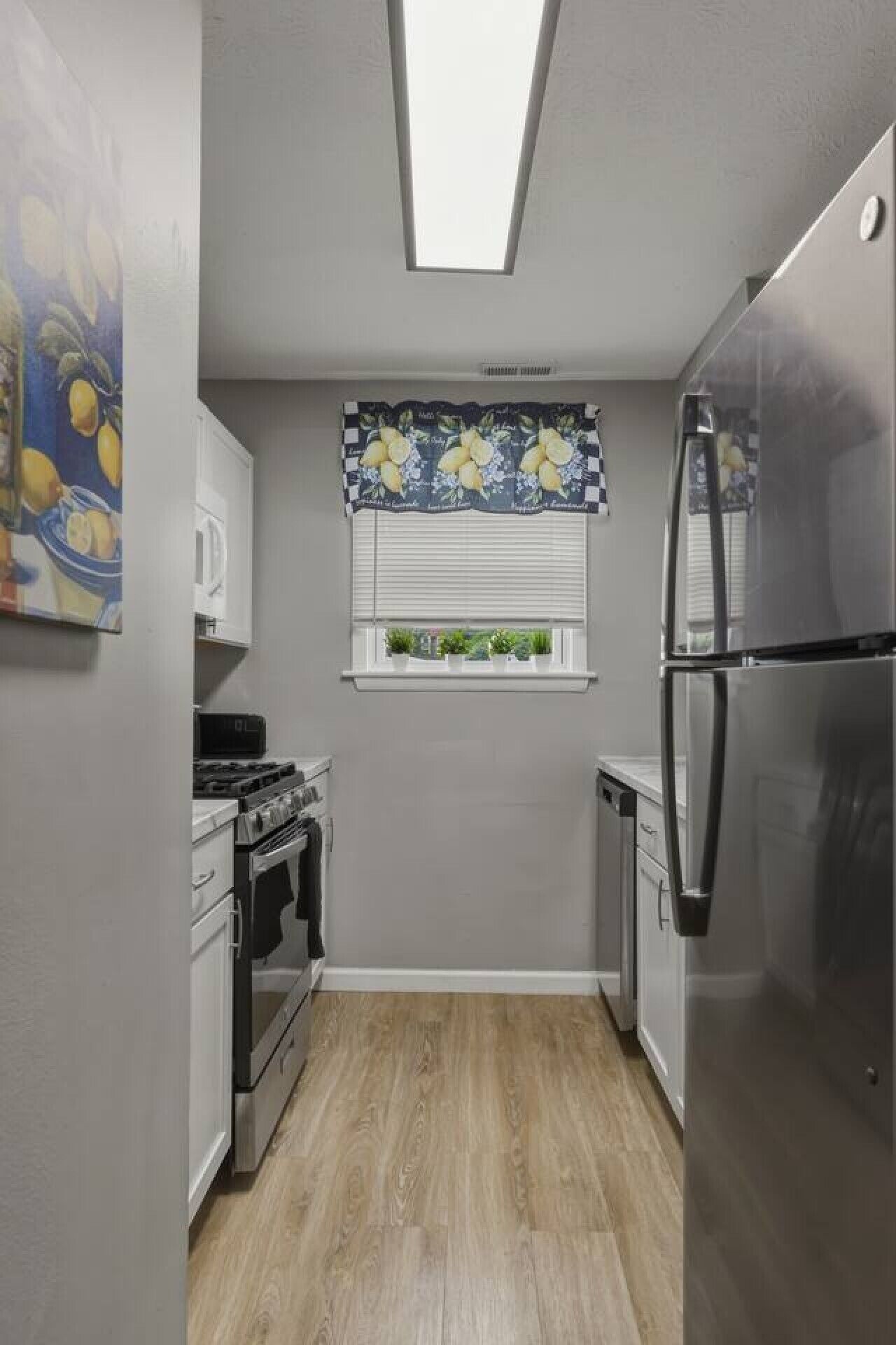 A compact kitchen with a built-in oven, a refrigerator, and a window with a floral curtain.