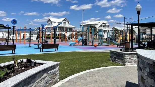 A playground with slides and climbing structures, benches, and a building with a white facade in the background. - Golf + Beach stay w/ private putting green! (Shallotte)