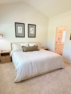 A bedroom with a bed, two nightstands, a bedside lamp, and a door leading to a bathroom. - Golf + Beach stay w/ private putting green! (Shallotte)