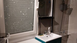 Een badkamer met een raam, een wastafel, een spiegel en een douche.