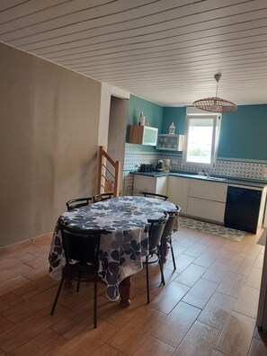 A dining area with a round table, chairs, a kitchen with a window, and a ceiling fan. - townhouse (plouezec)