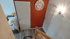 Een trap met een houten leuning die leidt naar een kamer met een witte deur en een wandklok.