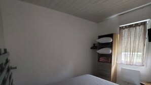 Een eenpersoonskamer met houten plafond, raam met gordijnen, bureau en stoel.