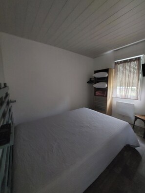 A single-bed room with a wooden ceiling, a window with curtains, a desk, and a chair. - townhouse (plouezec)