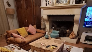 A living room with a fireplace, a sofa, a coffee table, and a television. - Provençal villa with a private pool, shaded garden terrace, quiet location, and parking (Arles)