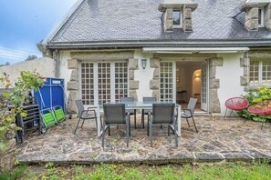 Ein Steinhaus mit Terrasse, einem Esstisch mit Stühlen und einem kleinen Garten.