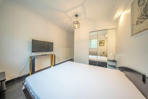 Ein modernes Hotelzimmer mit einem großen Bett, einem Flachbildfernseher, einem Nachttisch und einem Spiegel.