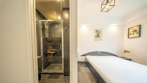 Un dormitorio con cama, mesita de noche, cuadro enmarcado y zona de ducha.