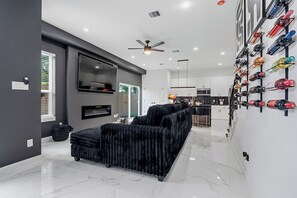A modern living room with a black sofa, a ceiling fan, and a wall-mounted shoe rack. - Luxury 3BR Near Downtown, NRG & Med Center (Houston)