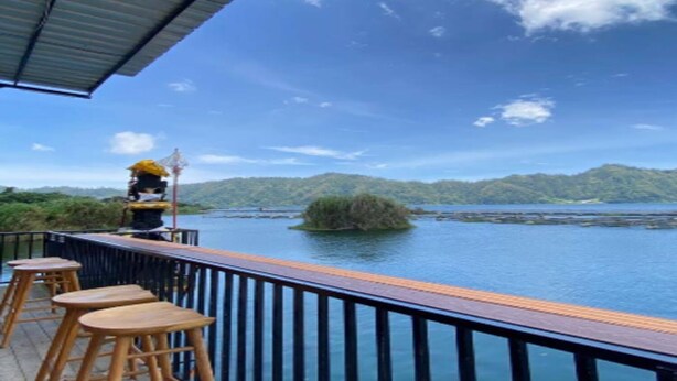 Une terrasse avec des tabourets en bois, donnant sur une étendue d’eau et une colline boisée.