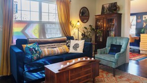 A living room with a blue sofa, a wooden coffee table, a blue armchair, a lamp, and a bookshelf. - Artist's bungalow and garden in SE Portland (Milwaukie)