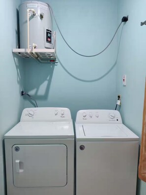 Ein Waschbereich mit zwei weißen Waschmaschinen und einem Warmwasserbereiter an einer hellblauen Wand.