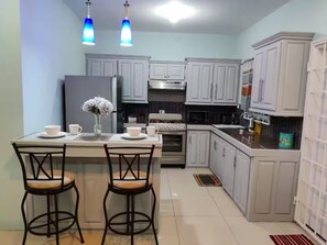 A kitchen with white cabinets, a stove, a refrigerator, and two bar stools. - Marvelous 1-bedroom apartment with AC in St Helena (St Helena)