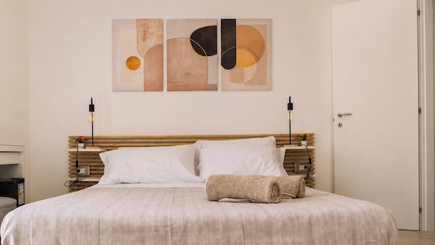 A neatly made bed with a wooden headboard, two bedside lamps, and a wall art piece above. - GEA Guest House (Syracuse)