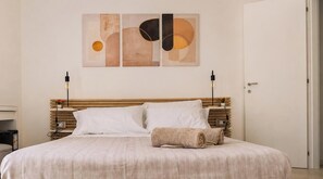 A neatly made bed with a wooden headboard, two bedside lamps, and a wall art piece above. - GEA Guest House (Syracuse)