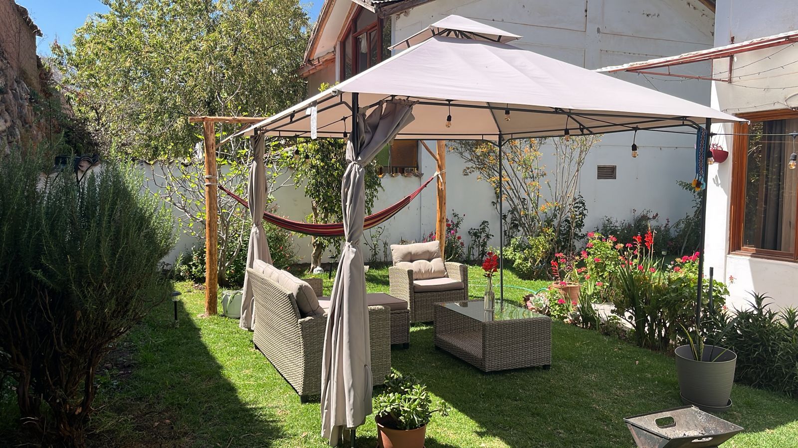 Un espace extérieur aménagé, abrité et doté de mobilier en osier, d’un hamac et de plantes en pot.