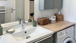 Moderni kylpyhuone, jossa on pesuallas, peili, riippuvalaisimet ja pesukone.