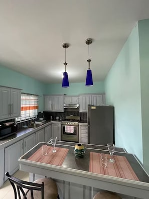Eine Küche mit weißen Schränken, einem Herd, einem Kühlschrank und zwei blauen Pendelleuchten.