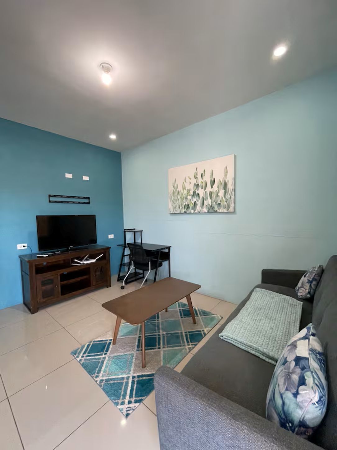 Un salon avec un téléviseur, un bureau, un canapé et un tableau accroché au mur.
